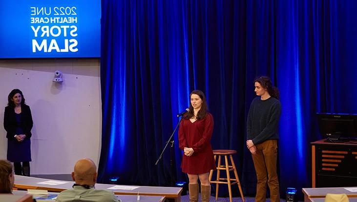 Two presenters stand on a stage at U N E's healthcare story slam event