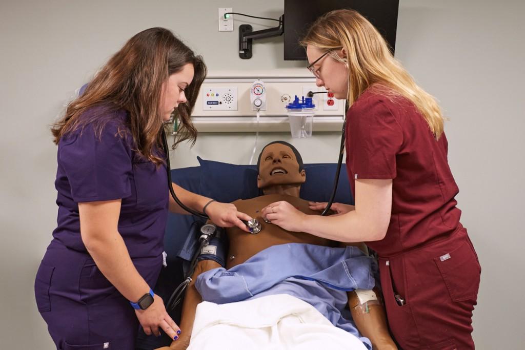 Two P A students use stethoscopes to listen to cardiac sounds from a patient simulator