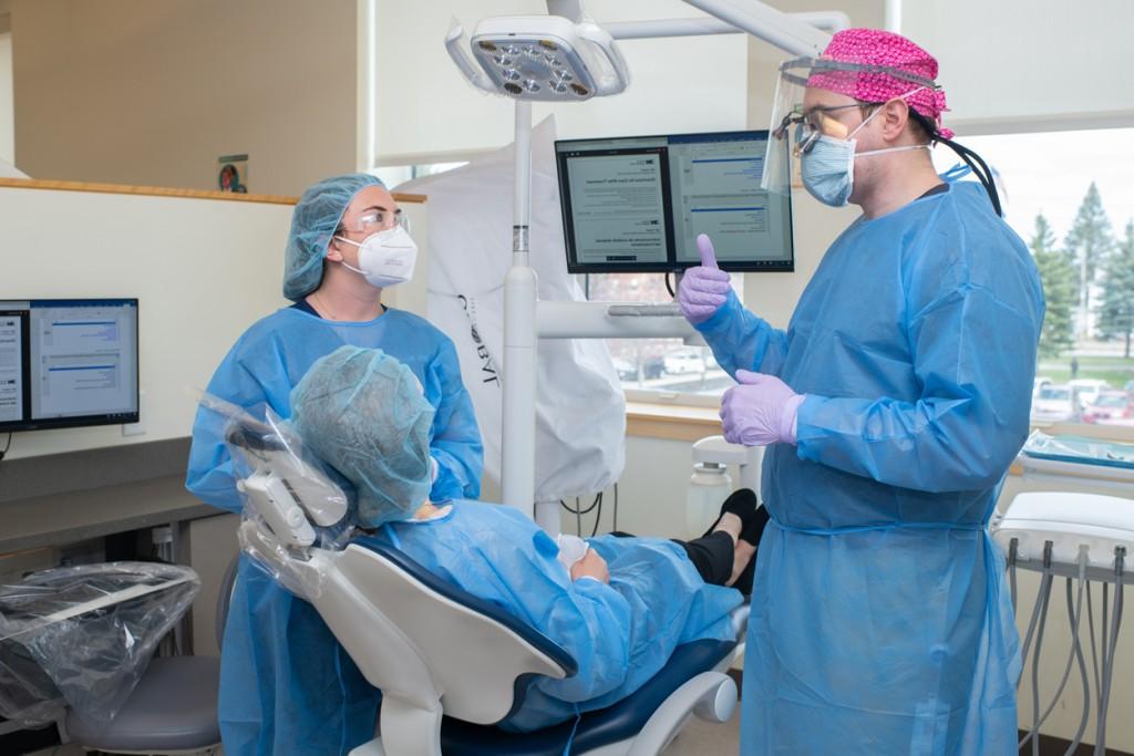 A 牙科 student 和 a P A student in blue scrubs discuss 牙科 work with a patient