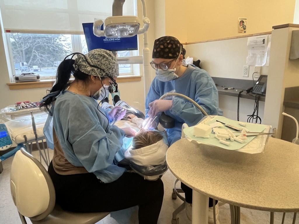 Two dental students clean a patient's teeth in the oral health clinic