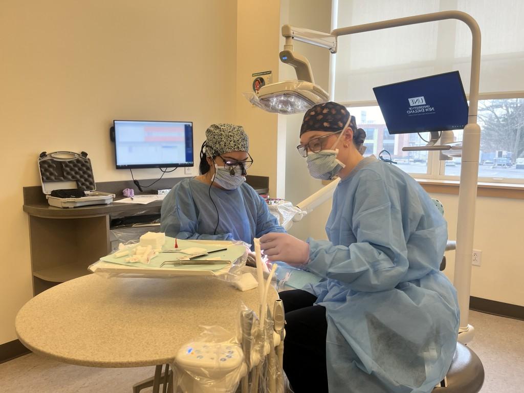 Two dental students clean a patient's teeth in the oral health clinic