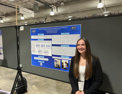 A UNE student poses in front of a research poster