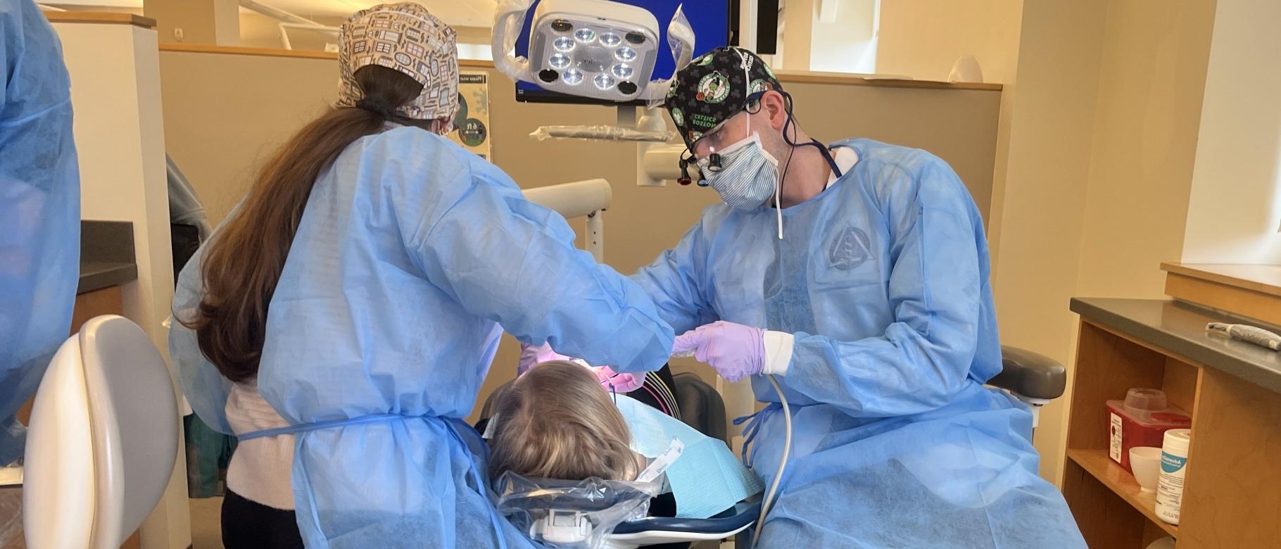 Two dental students clean a patient's teeth in the oral health clinic