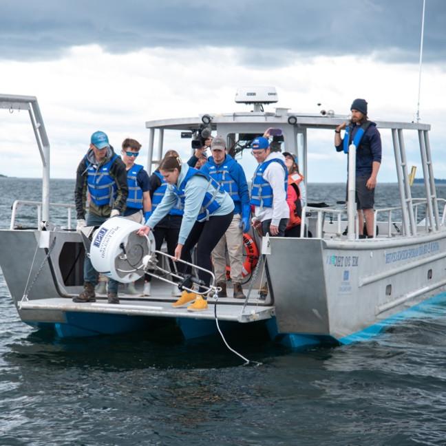 A group of students on a U N E boat retreive a white shark buoy from the ocean