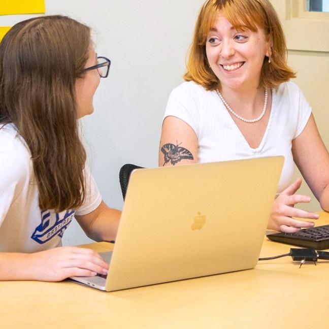 Two computer science students talk in front of a laptop