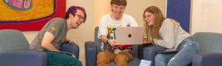 Three University of New England students sit together around a laptop