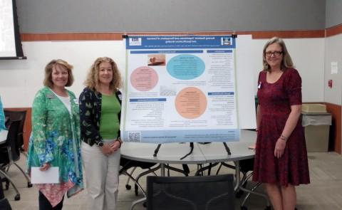 Three UNE faculty members stand 下一个 to a research poster