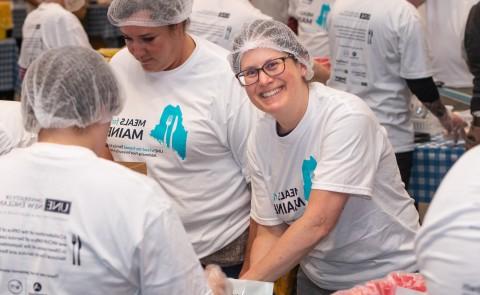 A volunteer smiles through the crowd of others helping to pack meal kits for the Meals for Maine event