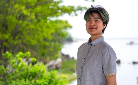 A UNE student poses in front of the Saco River on UNE's campus