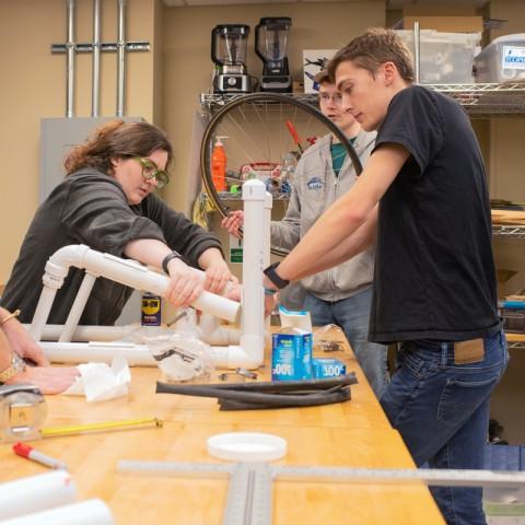 Three students and a professor assemble part of a wheelchair together